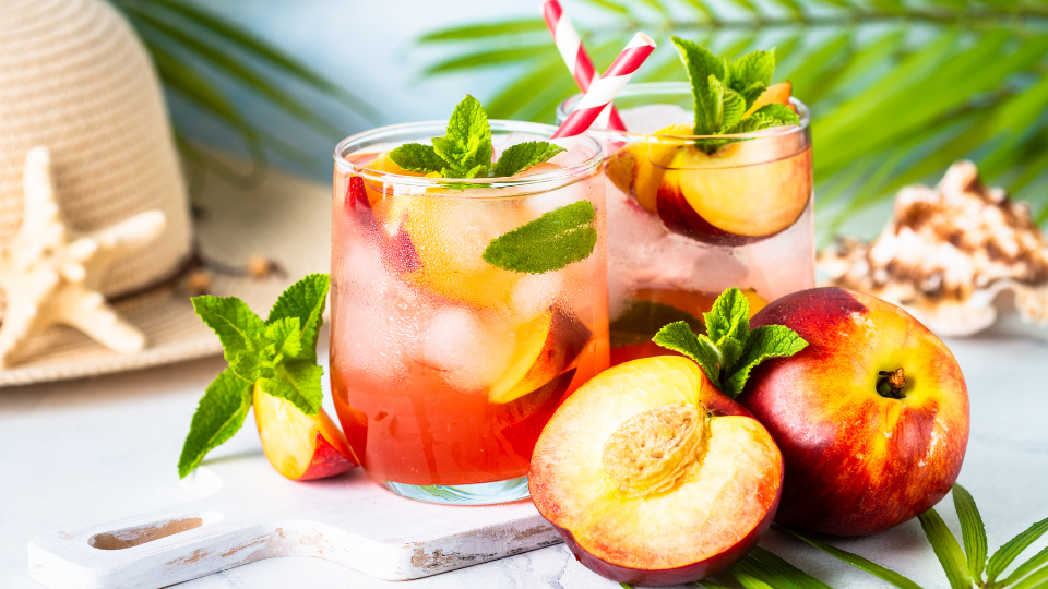 Iced tea with both cut and whole peaches around it. 