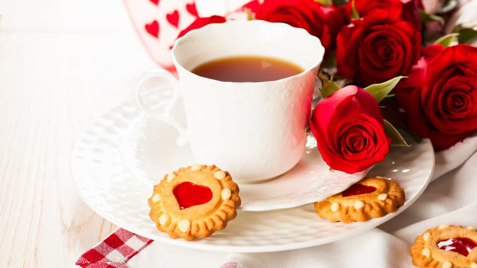 A cup of hot tea, heart cookies, and roses for Valentine's Day. 