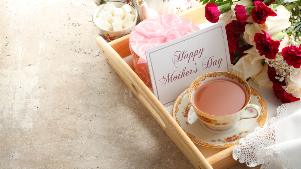 A wooden tray with flowers, a cup of hot tea, and a card that reads "Happy Mother's Day."